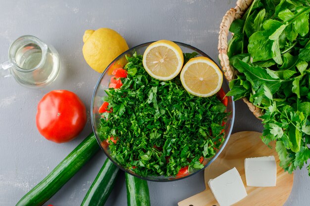 Conjunto de tomates, queso, limón, pepino y verduras picadas en un recipiente de vidrio sobre una superficie gris