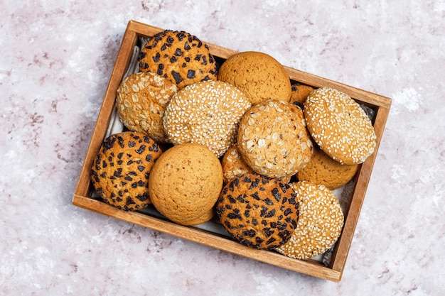 Conjunto de varias galletas de estilo americano en bandeja de madera sobre fondo de hormigón ligero. Galletas de mantequilla con semillas de sésamo, mantequilla de maní, avena y galletas de chispas de chocolate.