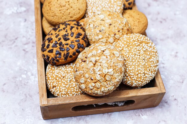 Conjunto de varias galletas de estilo americano en bandeja de madera sobre fondo de hormigón ligero. Galletas de mantequilla con semillas de sésamo, mantequilla de maní, avena y galletas de chispas de chocolate.