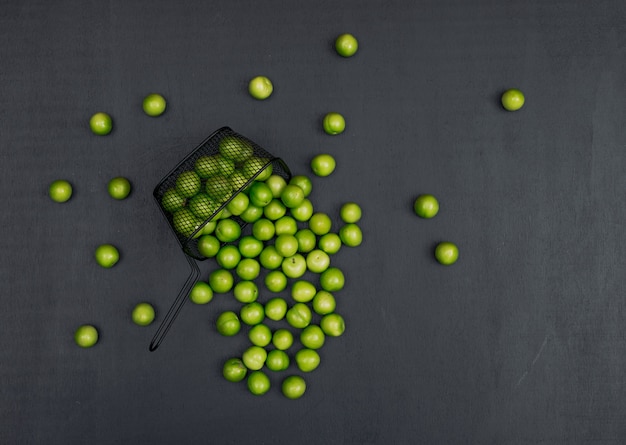 Conjunto de varios ciruela verde cereza alrededor y ciruela verde cereza en una cesta negra sobre un fondo negro. vista superior. espacio para texto