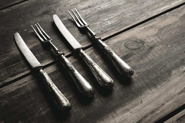 Conjunto vintage retro envejecido de tenedores y cuchillos de acero inoxidable cubiertos con pátina aislado en la vista lateral de la mesa de madera negra cepillada
