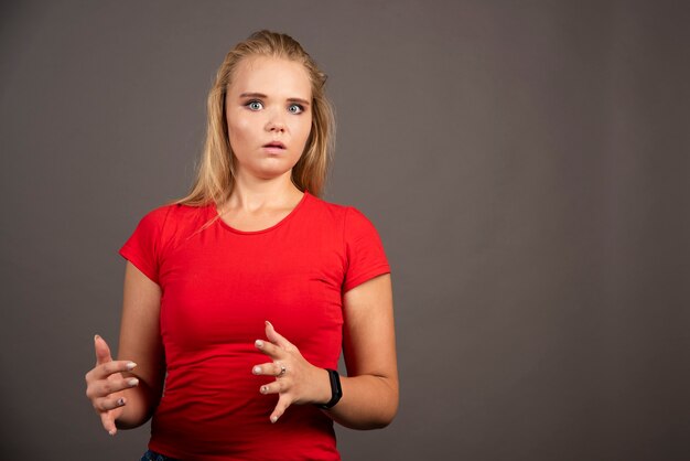 Conmocionada joven en camisa roja sobre pared negra.