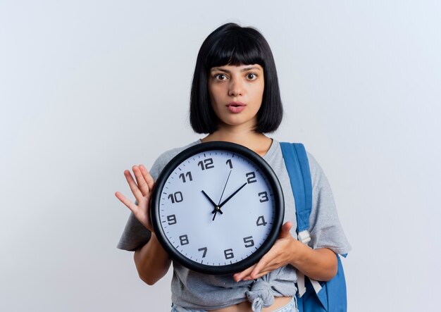 Conmocionada joven morena mujer caucásica con mochila tiene reloj