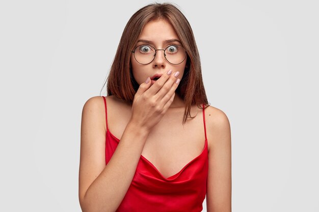 Conmocionada joven morena posando contra la pared blanca