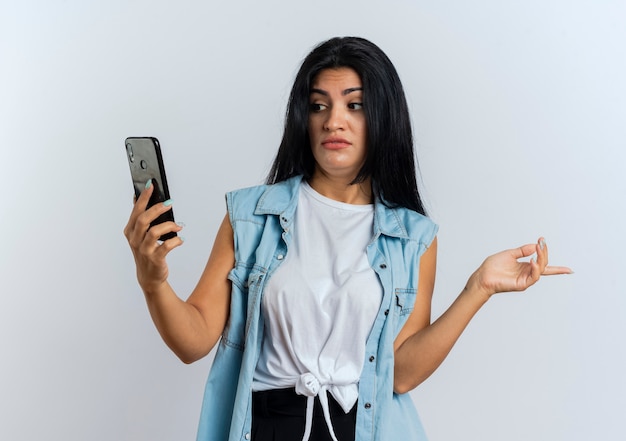 Conmocionada joven mujer caucásica mira el teléfono y señala al lado