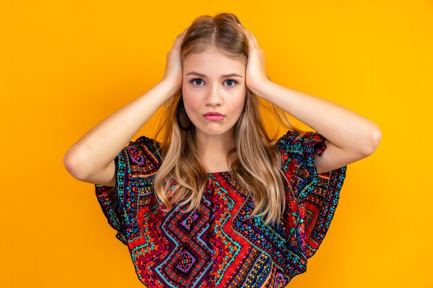 Conmocionada joven rubia poniendo las manos sobre su cabeza y mirando