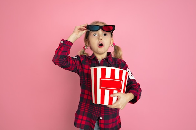 Conmocionada, jovencita sorprendida con palomitas de maíz y gafas 3D en pared rosa