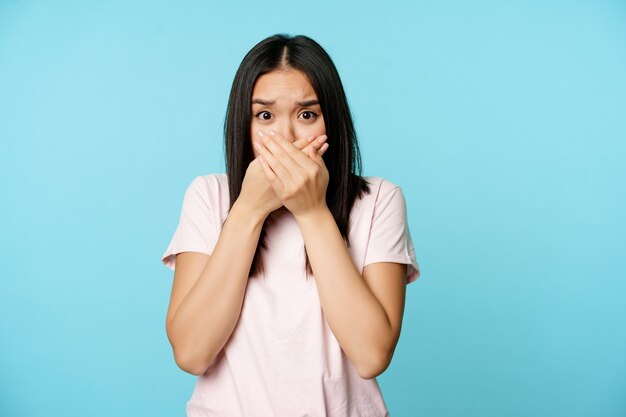 Conmocionada mujer asiática cubre la boca grita jadeando asustada asustada de algo cierra los labios de pie sobre ...