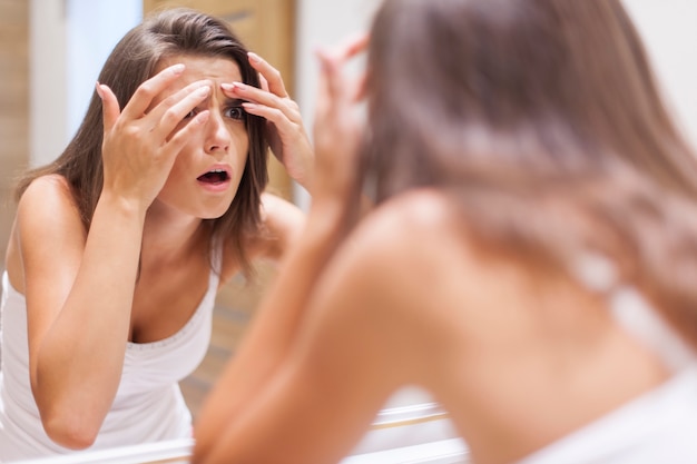 Conmocionada mujer exprimiendo la espinilla en el baño.