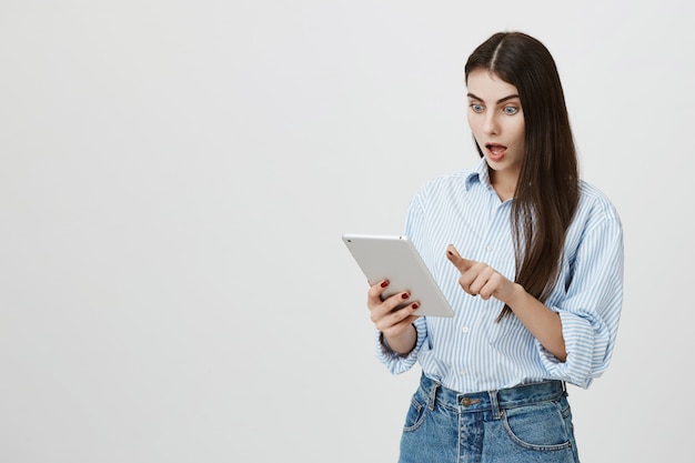 Conmocionada mujer mirando emocionado a la pantalla de la tableta digital