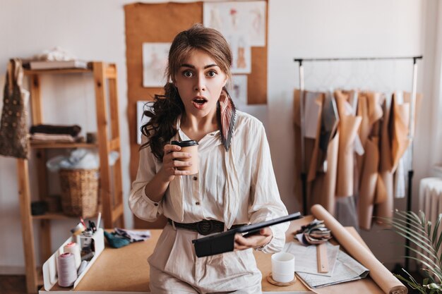 Conmocionada mujer tiene taza de café y tableta de computadora