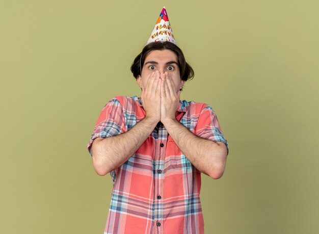 Foto gratuita conmocionado apuesto hombre caucásico vistiendo gorro de cumpleaños pone las manos en la boca