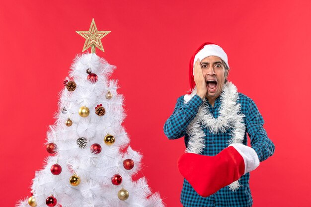 Conmocionado joven con sombrero de santa claus en una camisa azul a rayas y vistiendo su calcetín de Navidad