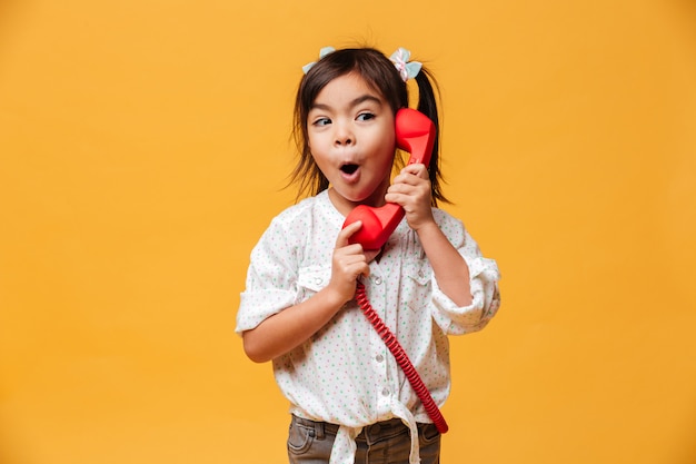 Conmocionado niña emocionada hablando por teléfono retro rojo.