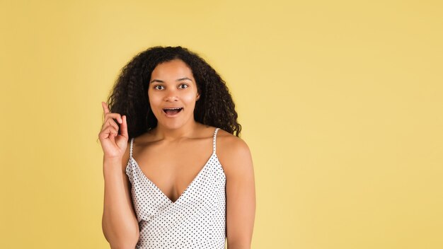 Conmocionado. Retrato de mujer hermosa afroamericana aislado en pared amarilla con copyspace. Modelo femenino con estilo. Concepto de emociones humanas, expresión facial, ventas, publicidad, moda, juventud.