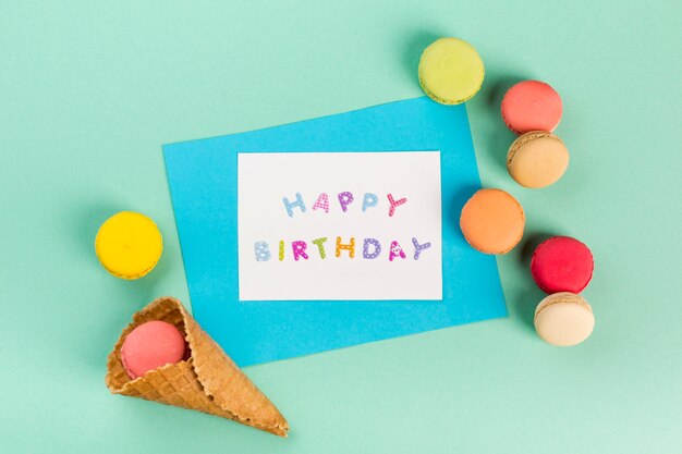 Cono de galleta con macarrones cerca de la tarjeta de feliz cumpleaños sobre fondo verde menta