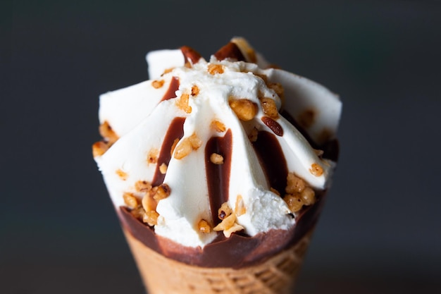 Cono de helado de crema y chocolate con avellanas y almendras sobre un fondo de color oscuro