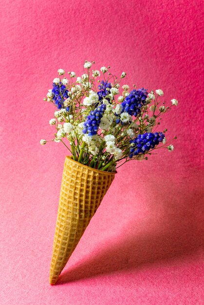 Cono de helado con flores en la pared rosa. Vista lateral, espacio de copia, concepto de flores de primavera