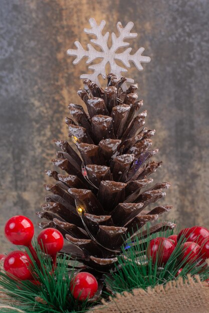 Cono de pino decorado con bayas de acebo y copo de nieve en el cuadro blanco.