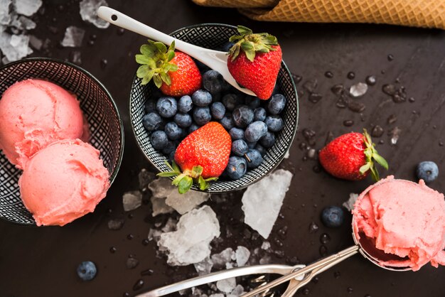 Cono de waffle cerca de bayas frescas y helado en los platos y una cuchara entre el hielo derretido