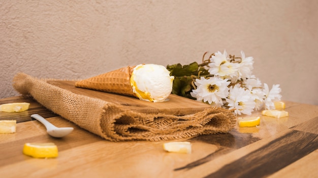 Cono de waffle con helado cerca de rodajas de frutas frescas y flores en la servilleta