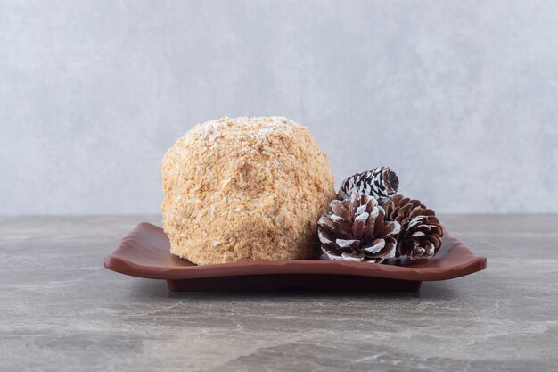 Conos de pino y un pastel de ardilla en un plato marrón sobre la superficie de mármol