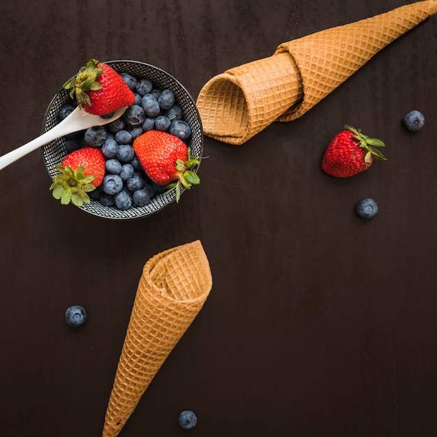 Conos de waffle cerca de bayas frescas en el plato y la cuchara