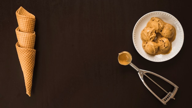 Conos de waffle cerca de bolas de helado en un plato y una cucharada