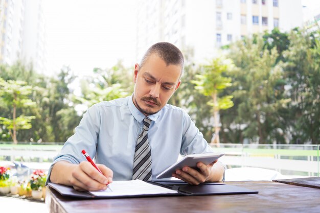 Consejero masculino concentrado editando datos en papel.