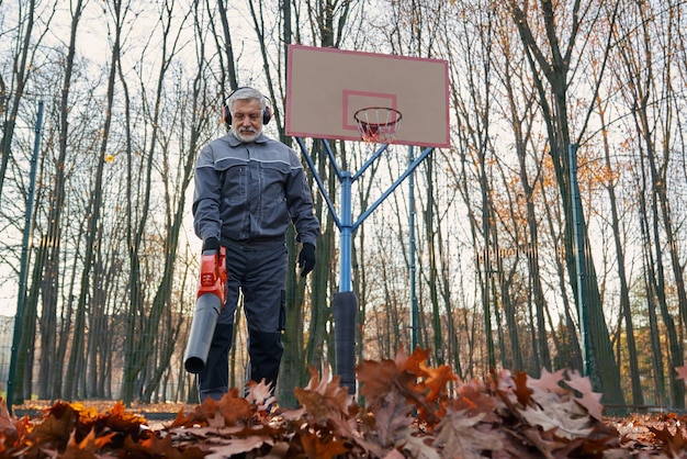 Foto gratuita conserje anciano cuidando el área del parque durante la temporada de otoño vista de ángulo bajo de un hombre barbudo con un mono