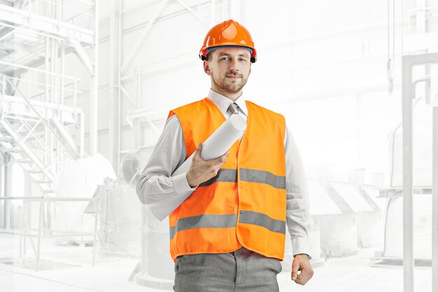 El constructor en un chaleco de construcción y un casco naranja de pie. Especialista en seguridad, ingeniero, industria, arquitectura, gerente, ocupación, empresario, concepto de trabajo