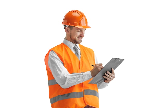 El constructor en un chaleco de construcción y casco naranja de pie sobre una pared blanca. Especialista en seguridad, ingeniero, industria, arquitectura, gerente, ocupación, empresario, concepto de trabajo