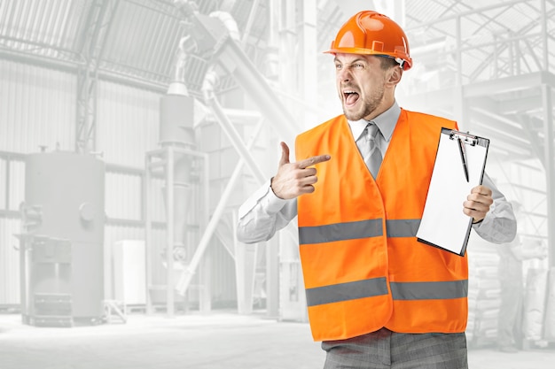 El constructor enojado con un chaleco de construcción y un casco naranja gritando. Especialista en seguridad, ingeniero, industria, arquitectura, gerente, ocupación, empresario, concepto de trabajo