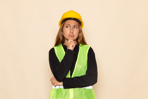 Foto gratuita constructor femenino de vista frontal en camisa negra casco amarillo posando pensando en la pared blanca