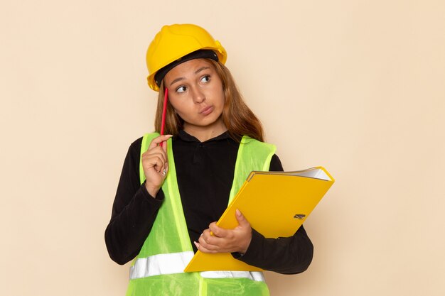 Constructor femenino de vista frontal en casco amarillo con archivo amarillo y lápiz pensando en escritorio blanco