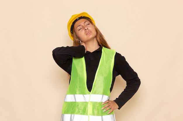 Foto gratuita constructor femenino de vista frontal en casco amarillo camisa negra posando con dolor de cuello en la pared blanca