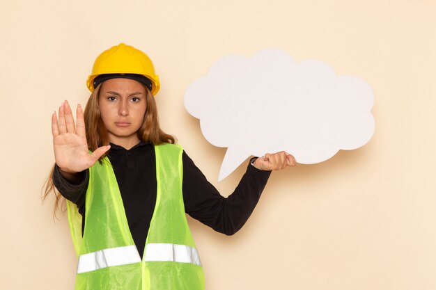 Constructor femenino de vista frontal en casco amarillo con cartel blanco en la pared blanca