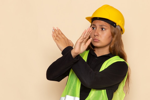 Foto gratuita constructor femenino de vista frontal en casco amarillo mostrando signo de prohibición en la pared blanca femenina