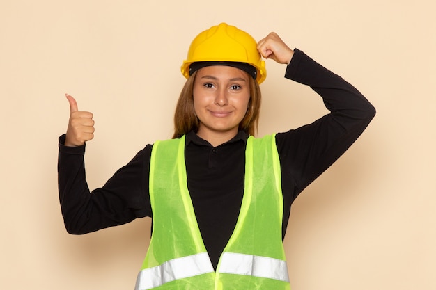 Constructor femenino de vista frontal en casco amarillo sonriendo mostrando como signo en la pared blanca