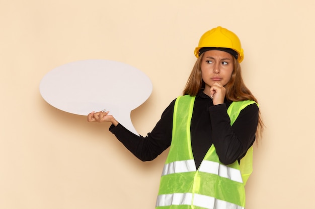Foto gratuita constructor femenino de vista frontal en casco amarillo sosteniendo un gran cartel blanco pensando en la pared blanca arquitecto femenino