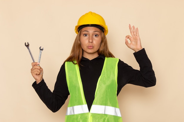 Constructor femenino de vista frontal en casco amarillo sosteniendo instrumentos de plata en la pared de luz arquitecto femenino