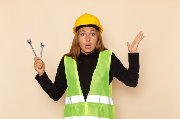 Constructor femenino de vista frontal en casco amarillo sosteniendo instrumentos plateados sorprendido en el escritorio ligero arquitecto femenino