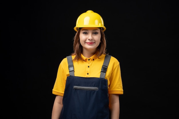 Foto gratuita constructor femenino de vista frontal en uniforme y casco protector en la pared negra