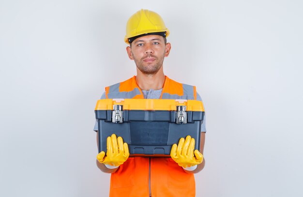 Constructor masculino con caja de herramientas de plástico en uniforme, casco, guantes, vista frontal.