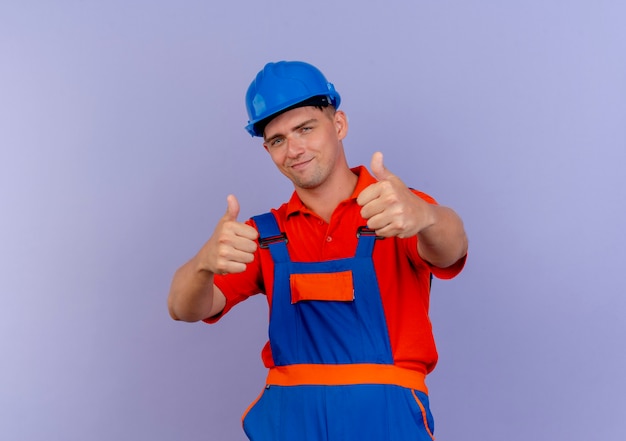 Constructor masculino joven complacido con uniforme y casco de seguridad con el pulgar hacia arriba en púrpura