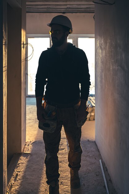 Un constructor masculino en ropa de trabajo con un casco protector en un sitio de construcción en pleno crecimiento.