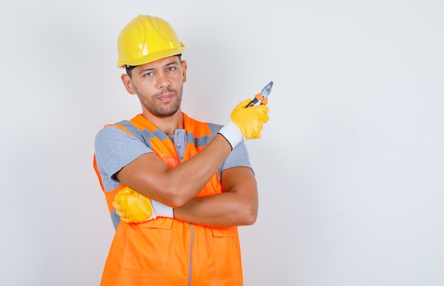 Constructor masculino en uniforme, casco, guantes con alicates, vista frontal.