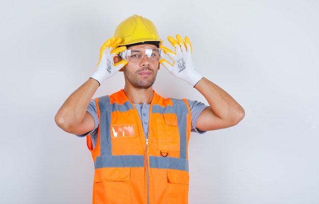 Constructor masculino en uniforme, casco, guantes con gafas de seguridad, vista frontal.