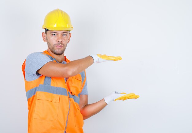 Constructor masculino en uniforme, casco, guantes con letrero de tamaño grande o pequeño, vista frontal.