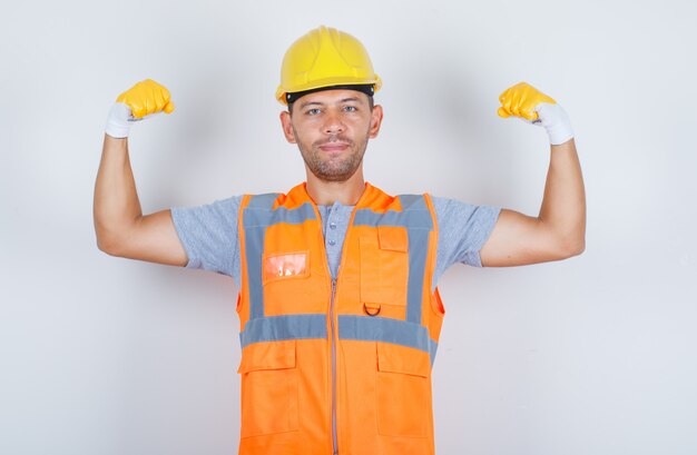 Constructor masculino en uniforme mostrando el músculo del brazo y sonriendo y luciendo fuerte, vista frontal.